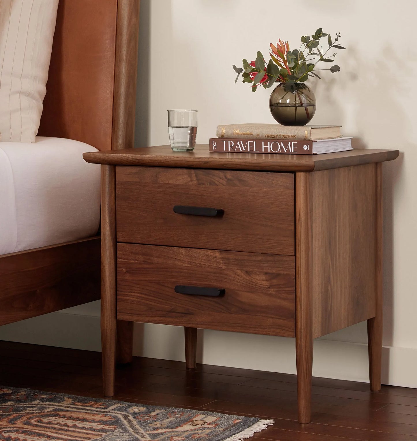 Mid century nightstand with double drawers, tapered legs, and black metal handles.