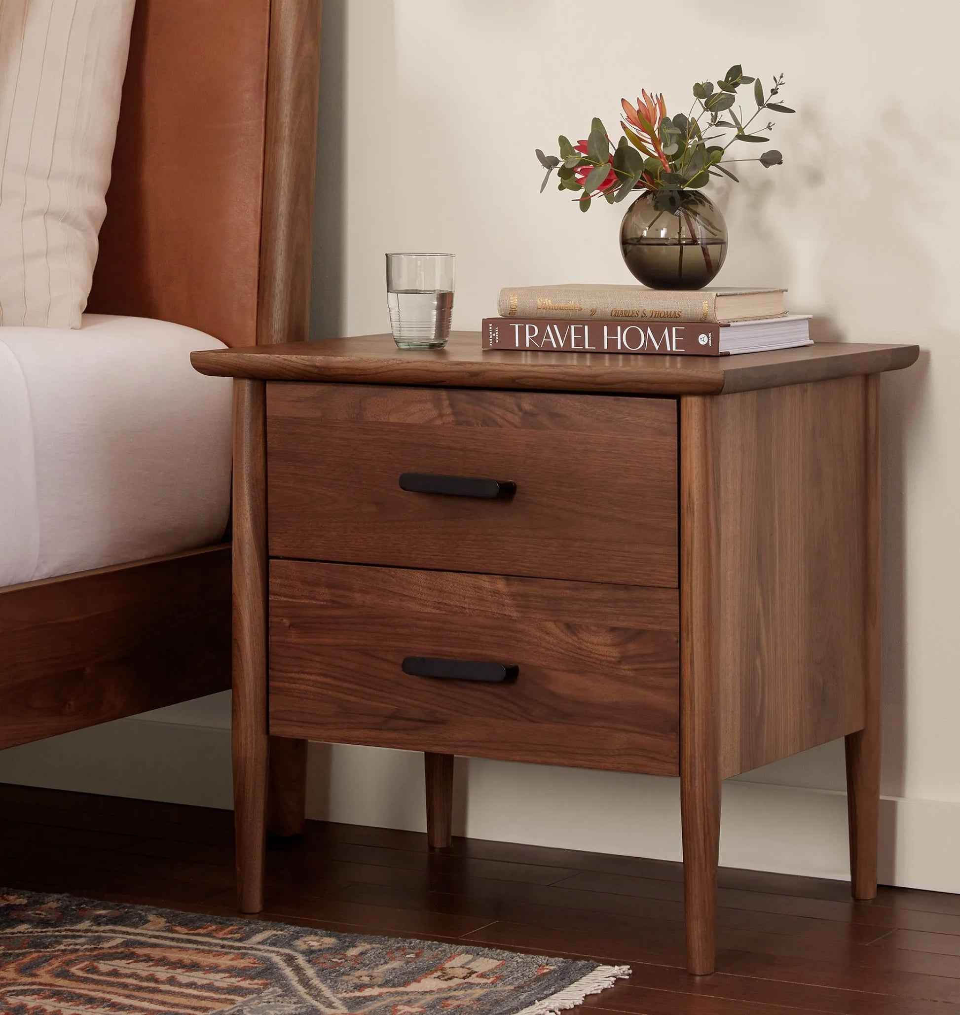 Mid century nightstand with double drawers, tapered legs, and black metal handles.