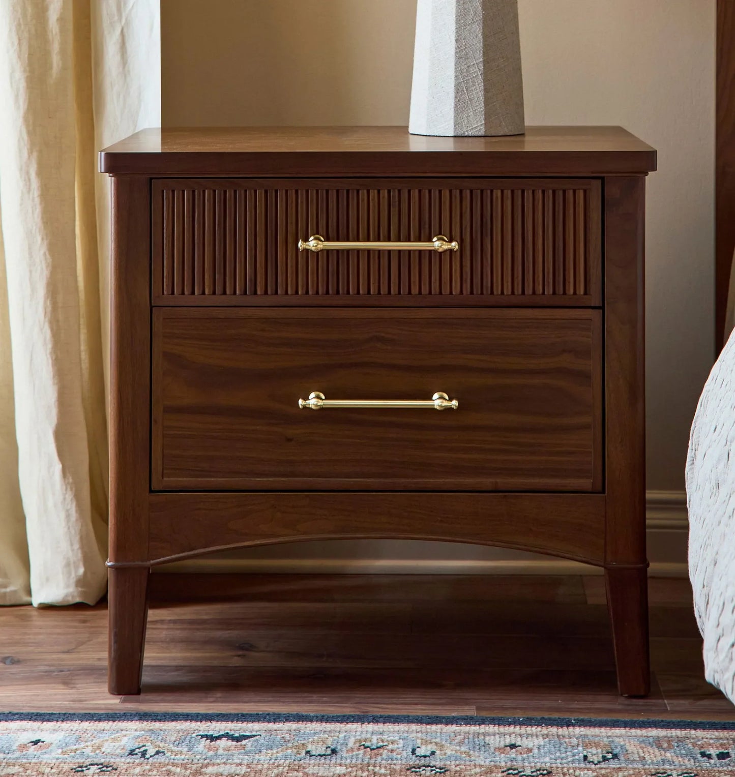 Mid century nightstand with ribbed drawer design, golden handles, and arched base.